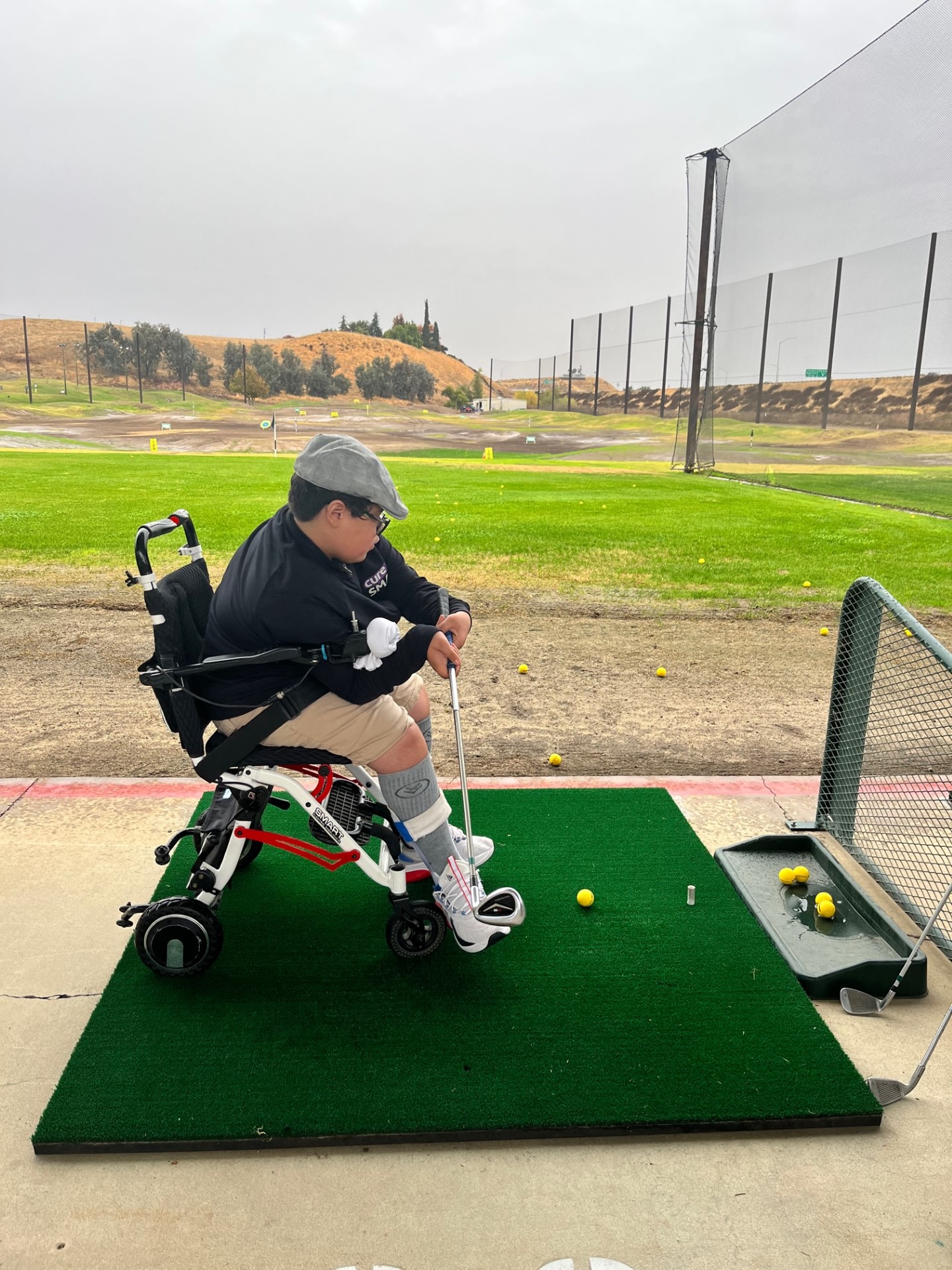 Am athlete sits in a wheelchair and swing a golf club at the ball, on the tee.