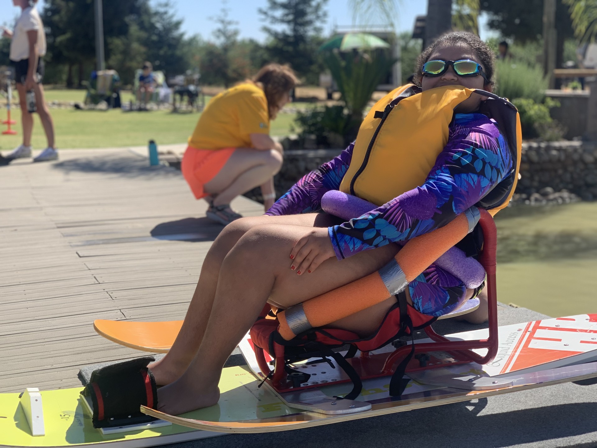 An athlete with goggles and a life jacket on sits in a sit ski, waiting to go.