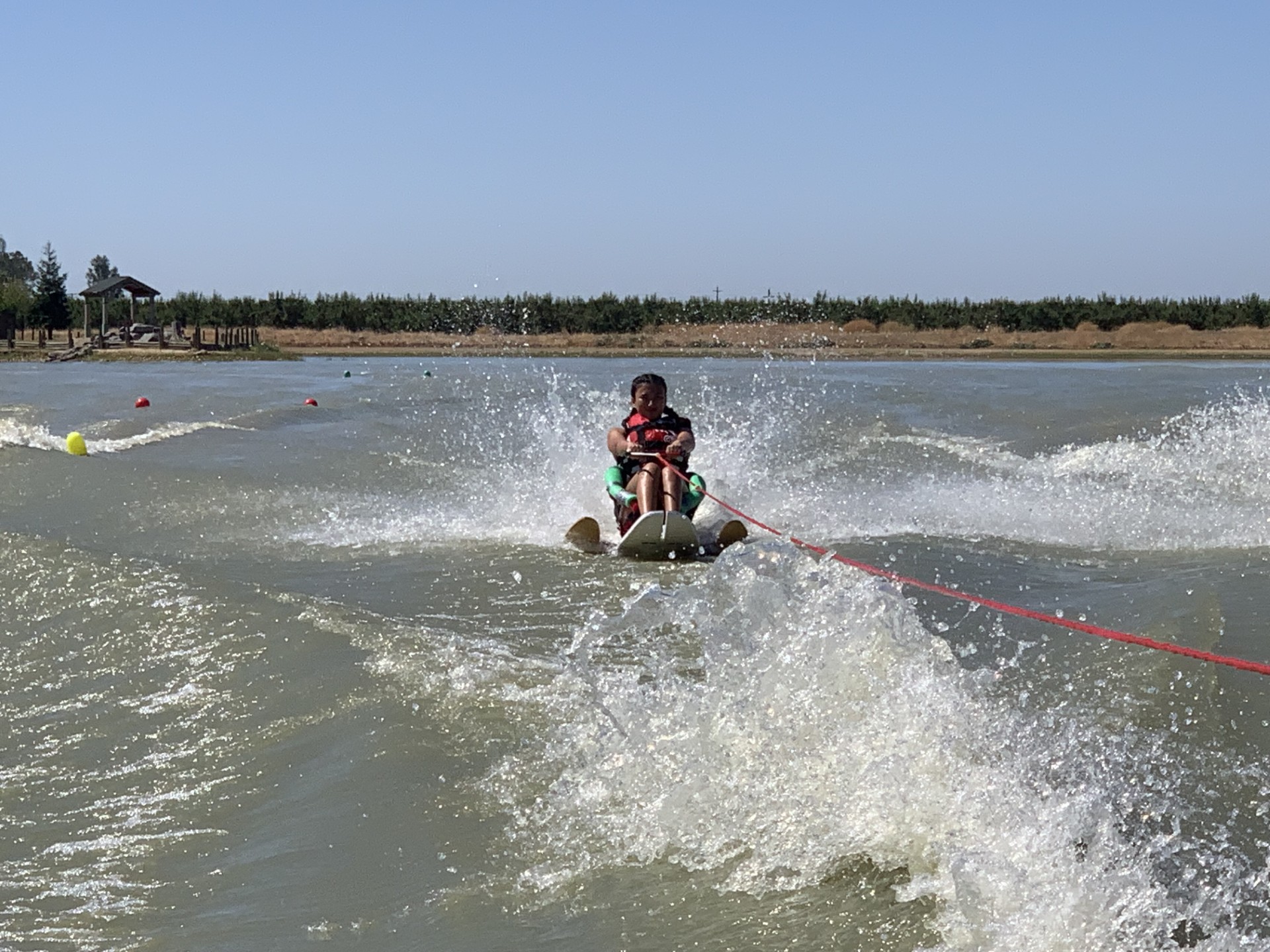 An athlete in a sit ski is towed behind a power boat on teh water.