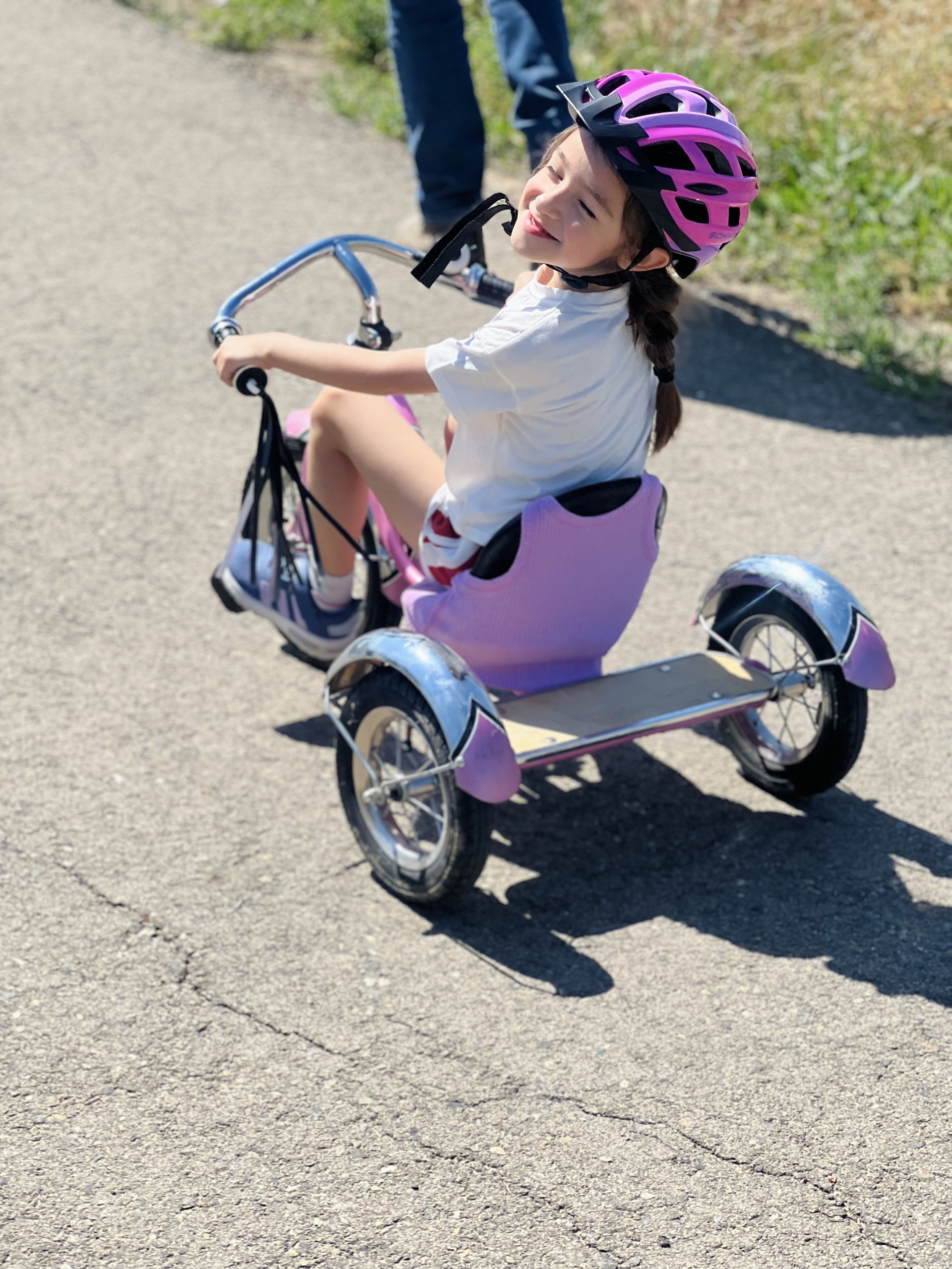 A young kid rides a three wheeled, purple bicycle, with a helmet on