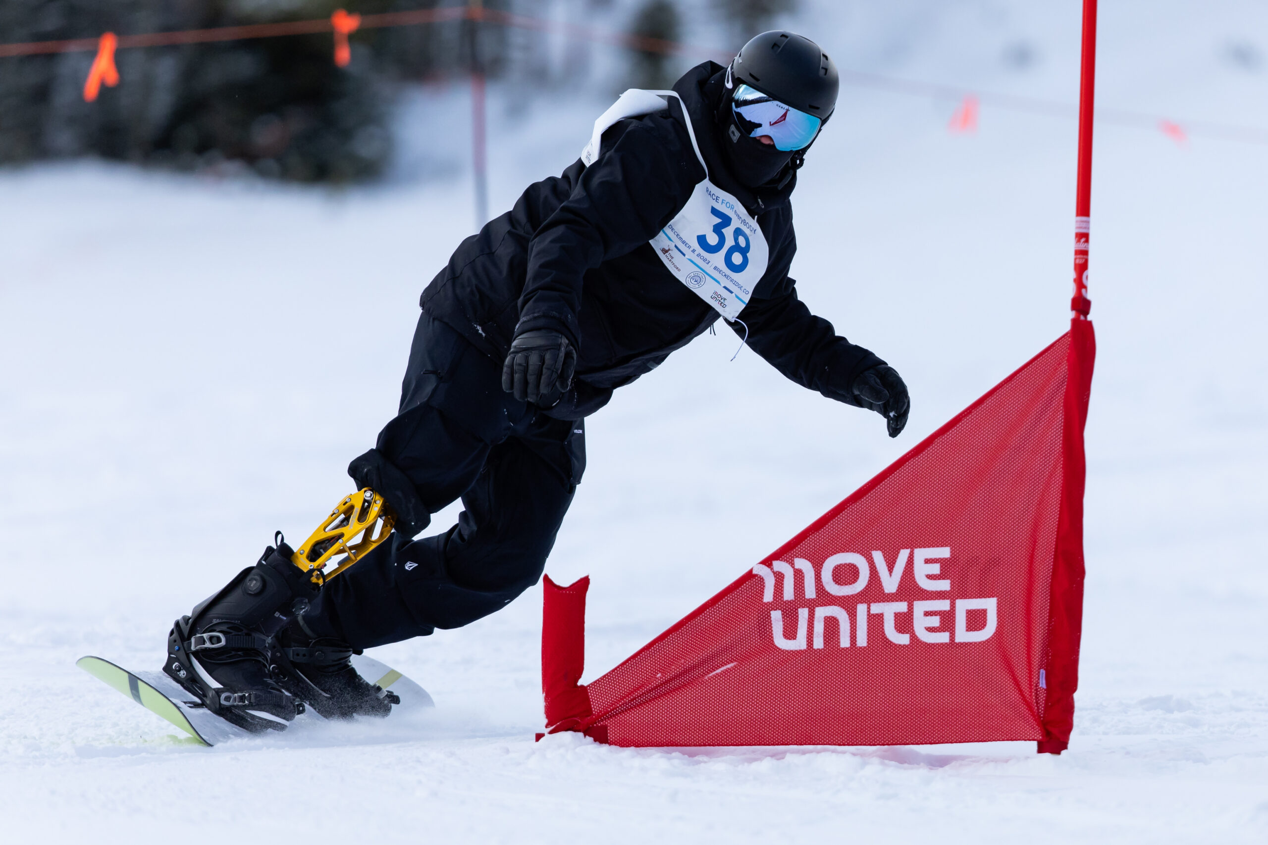 An athlete with a leg amputation snowboarding down a mountain around a Move United flag