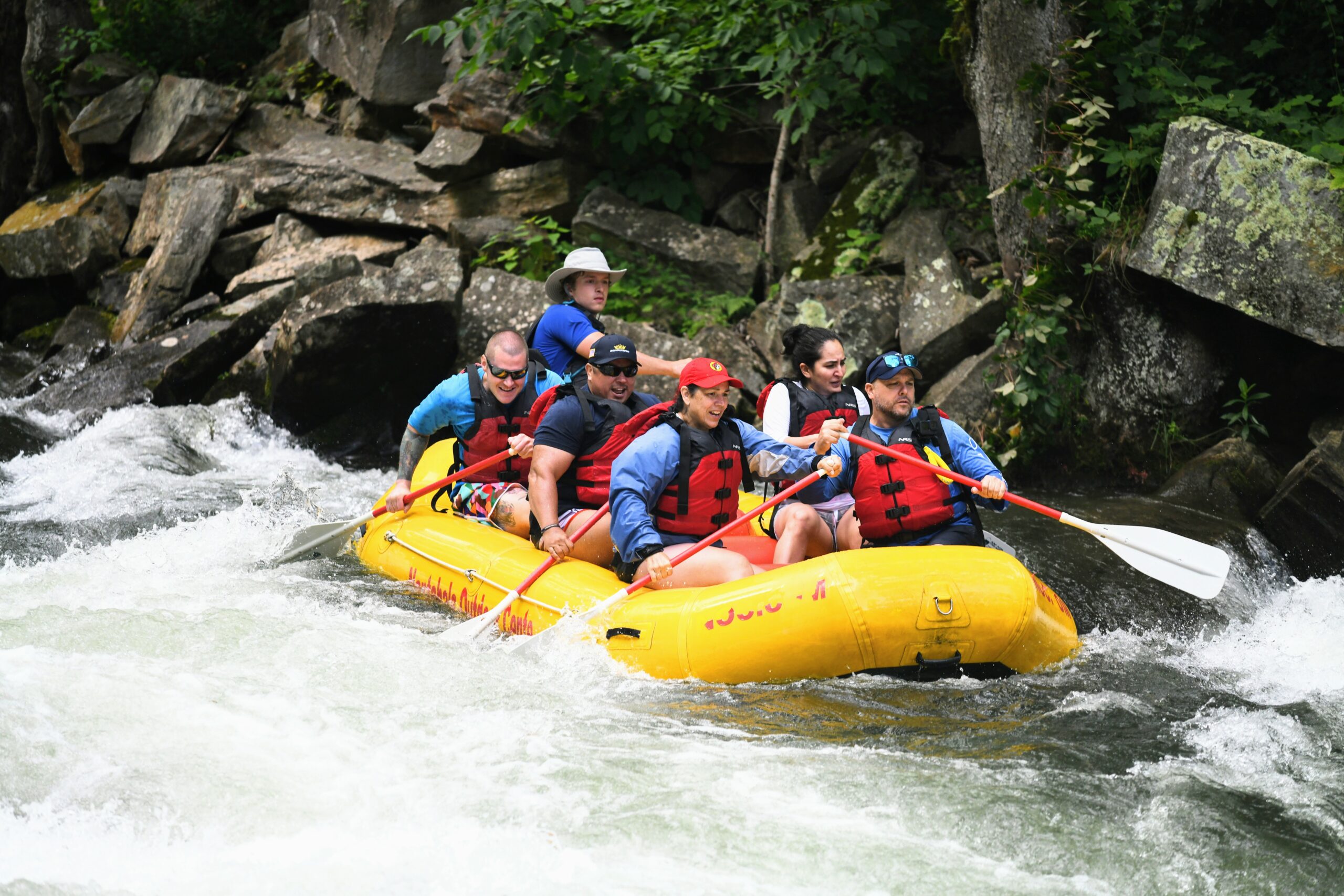 A group of individuals paddle a yellow raft down a white water section of a river