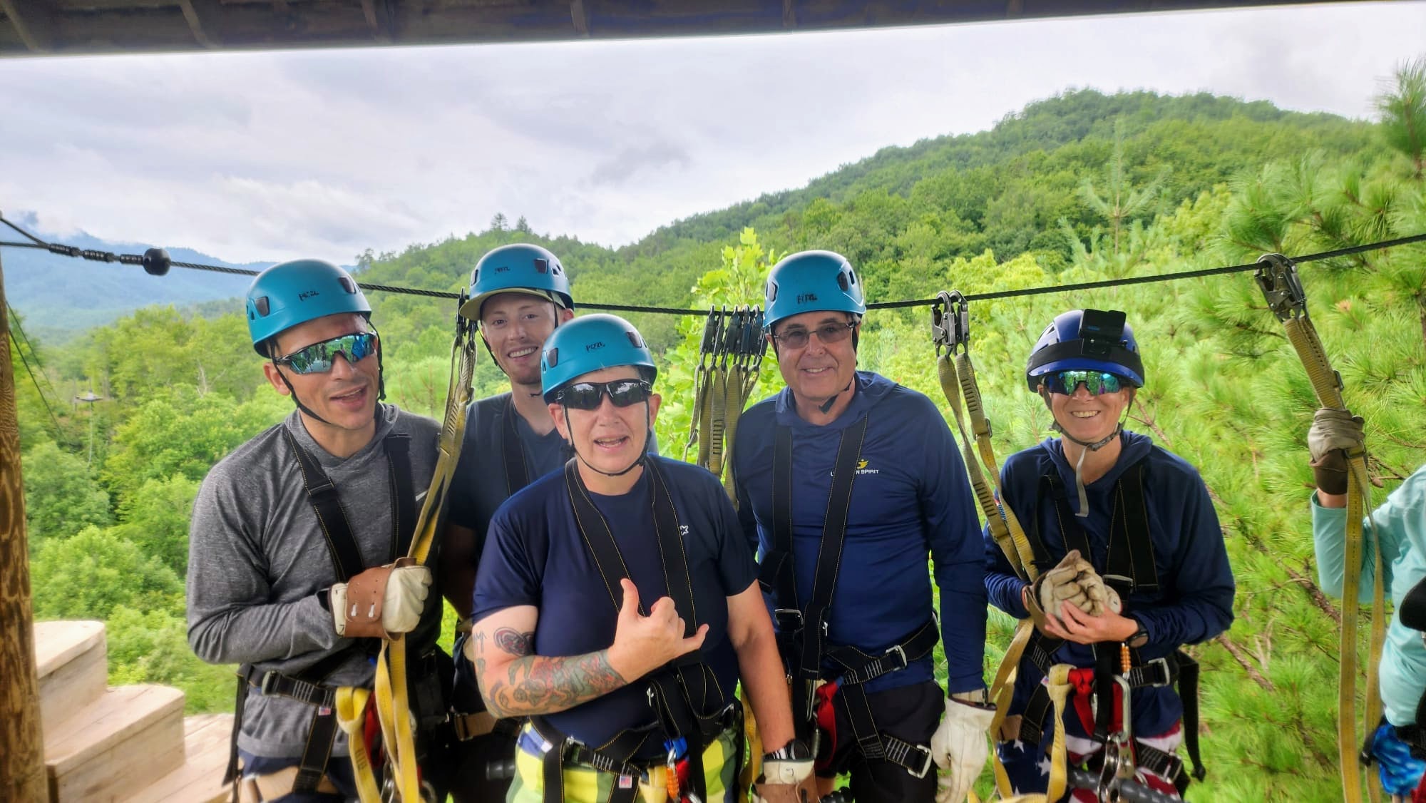 Group of Individuals smile for a picture while attached to a zipline on a platform.