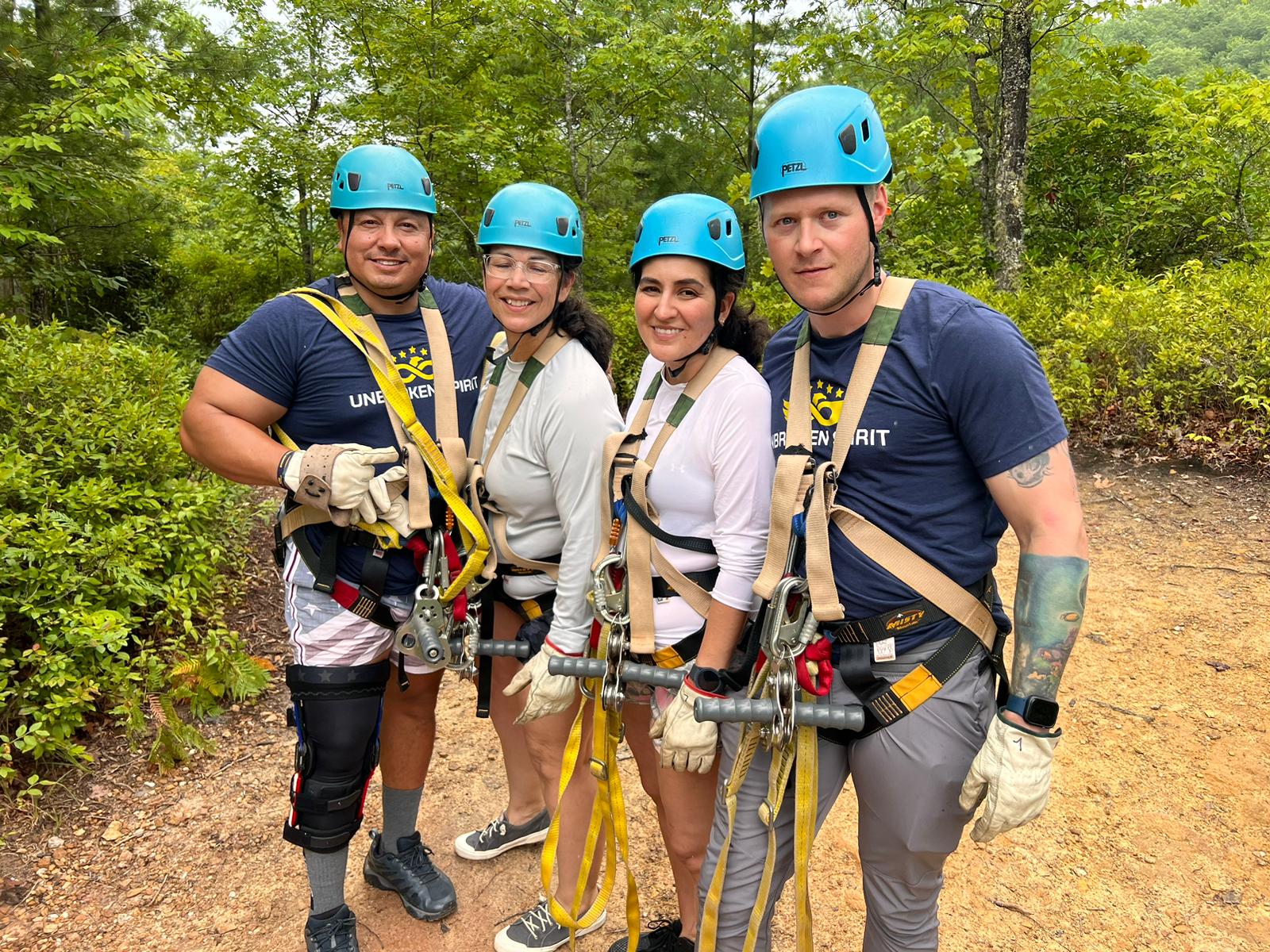 Four individuals smile for a picture with harnesses and helmets on.