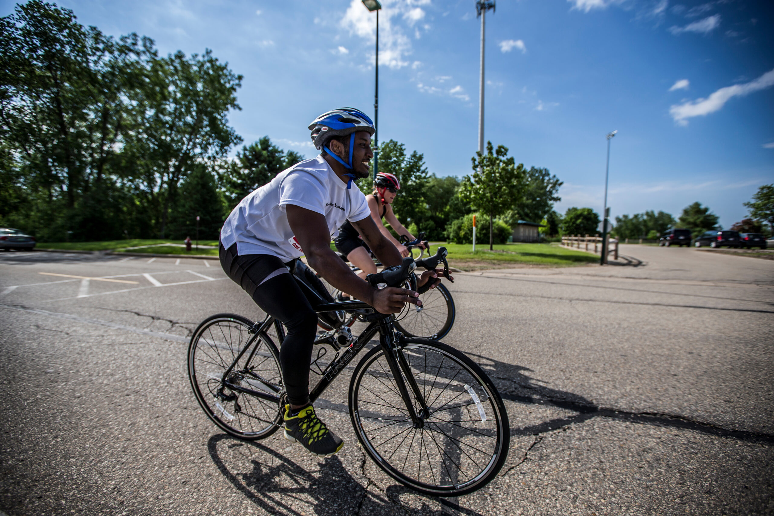 2 athletes smiling, clycling on a paved road as part of a triathlon training camp