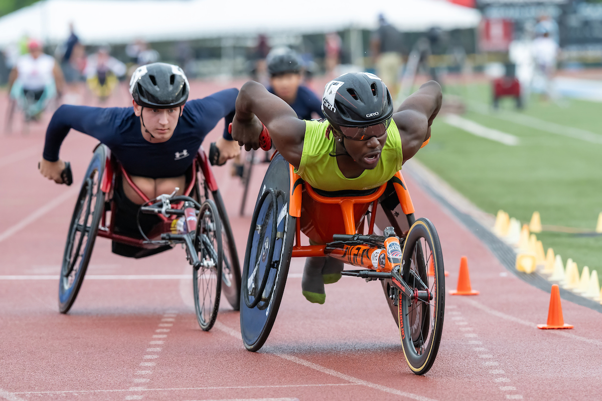 Two wheelchar track athletes turning corner of track in close proximity to one another