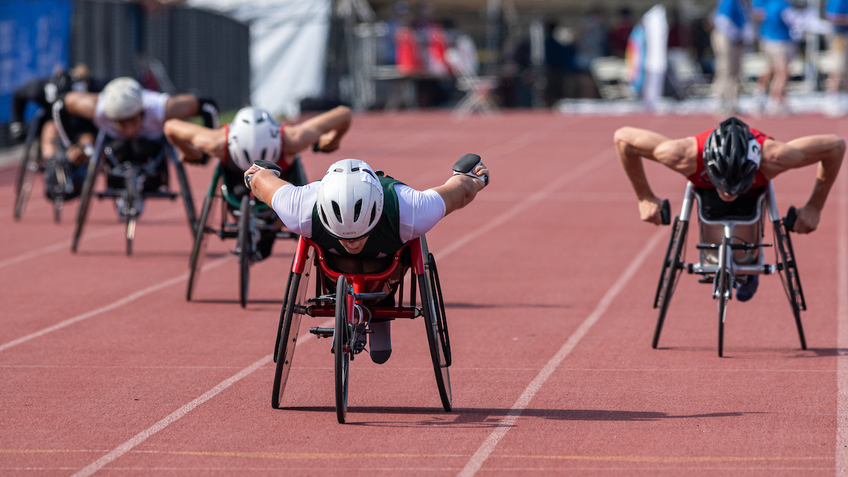 Several wheelchair raciers racing down long side of track in their respective lanes
