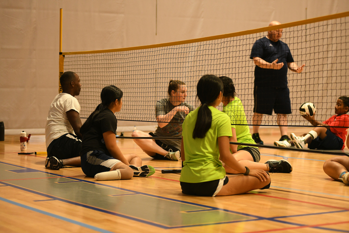 Several athletes seated on volleyball court listening to instructions from coach