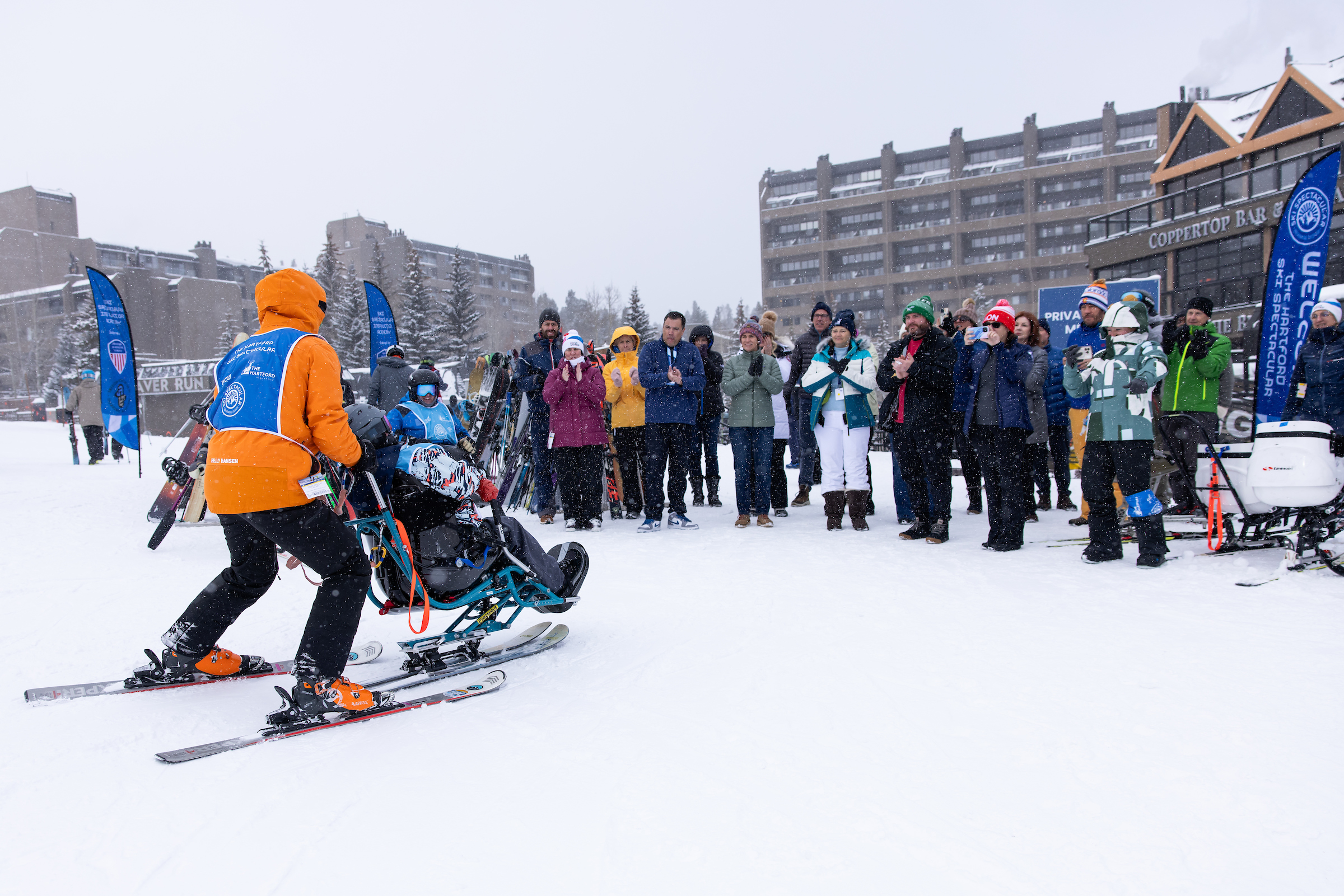 A skier and sit skier doing a demonstration of the sit ski in front of a group of individuals outdoors