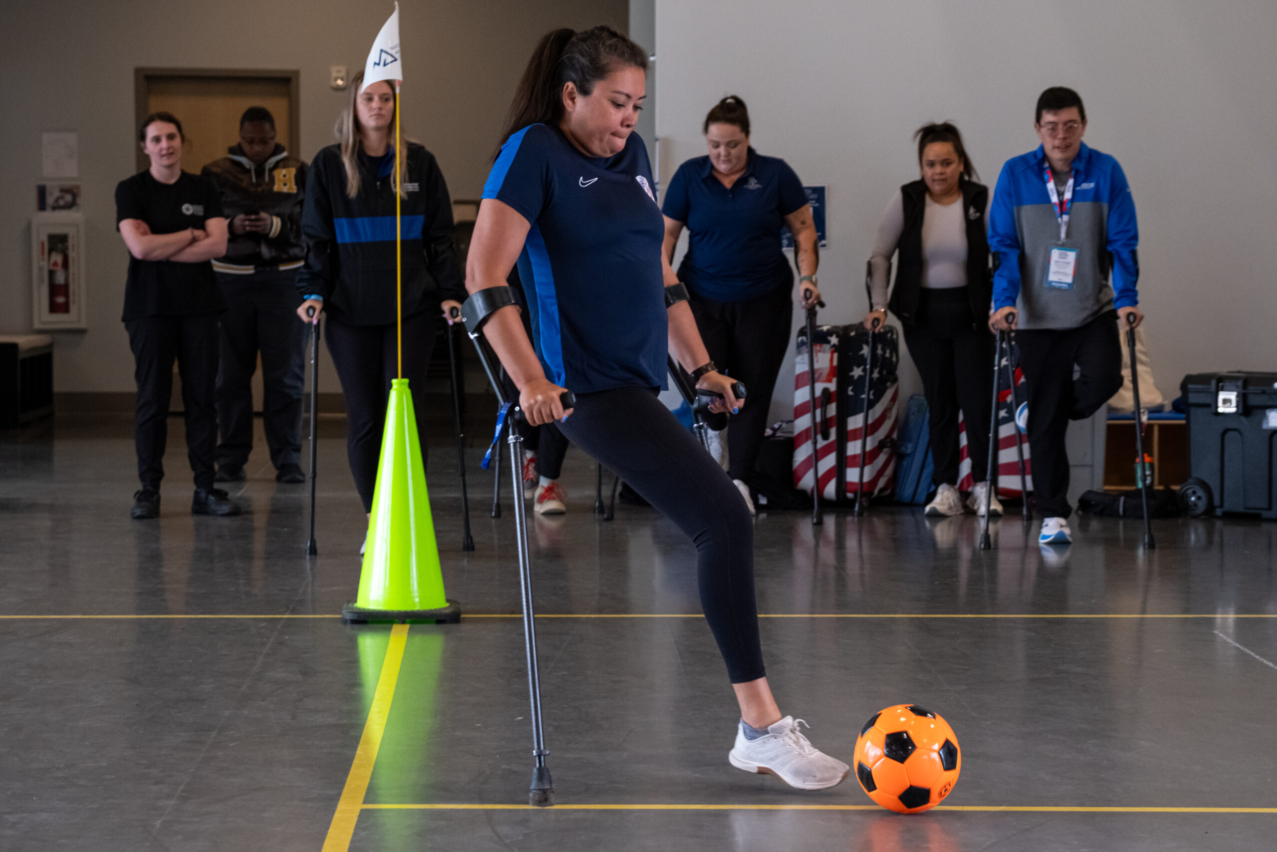 Amputee athlete demonstrating amputee soccer skills. Soccer ball is in front of athlete, athlete is preparing to kick the ball. Session participants are standing in the background observing the technique