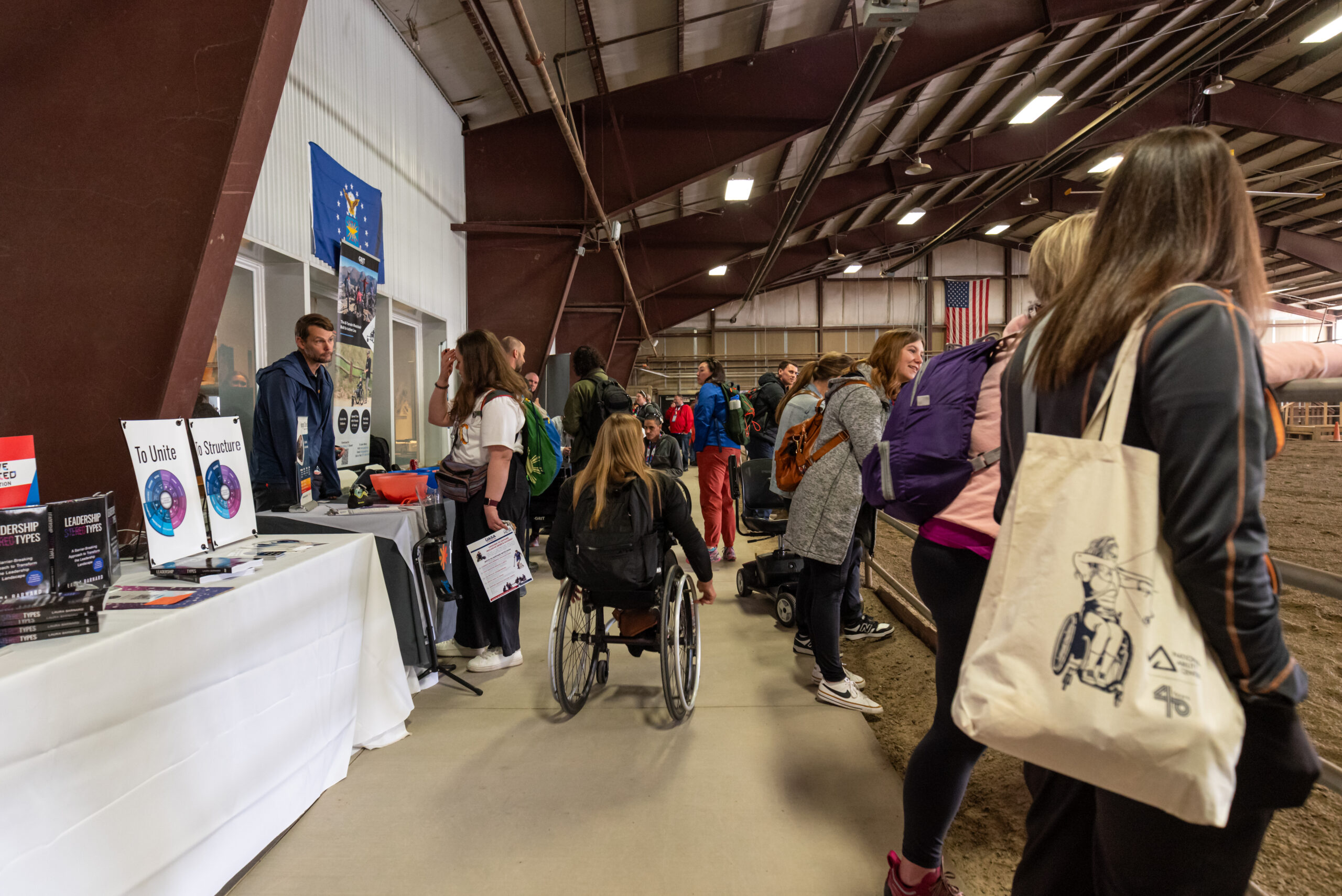 Distant view of exhibitor hallway at conference. Left side of image has exhibitor tables and attendees engaging with those exhibitors. Right side of image has attendees looking to the right into the nearby equestrian arena that borders the exhibitor hall