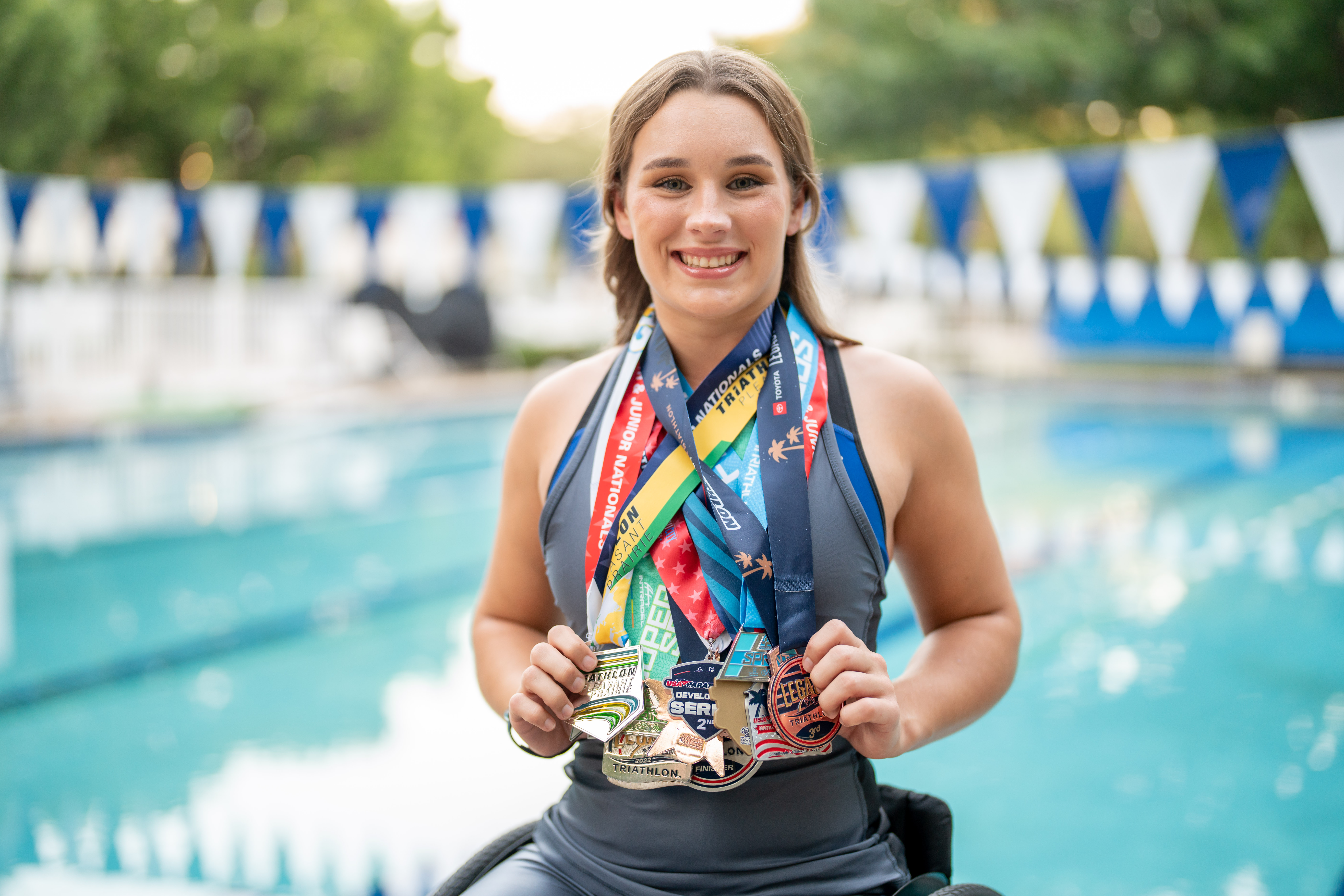 Skyler Fisher, a young female adaptive athlete smiling at a pool while displaying multiple medals around her neck.