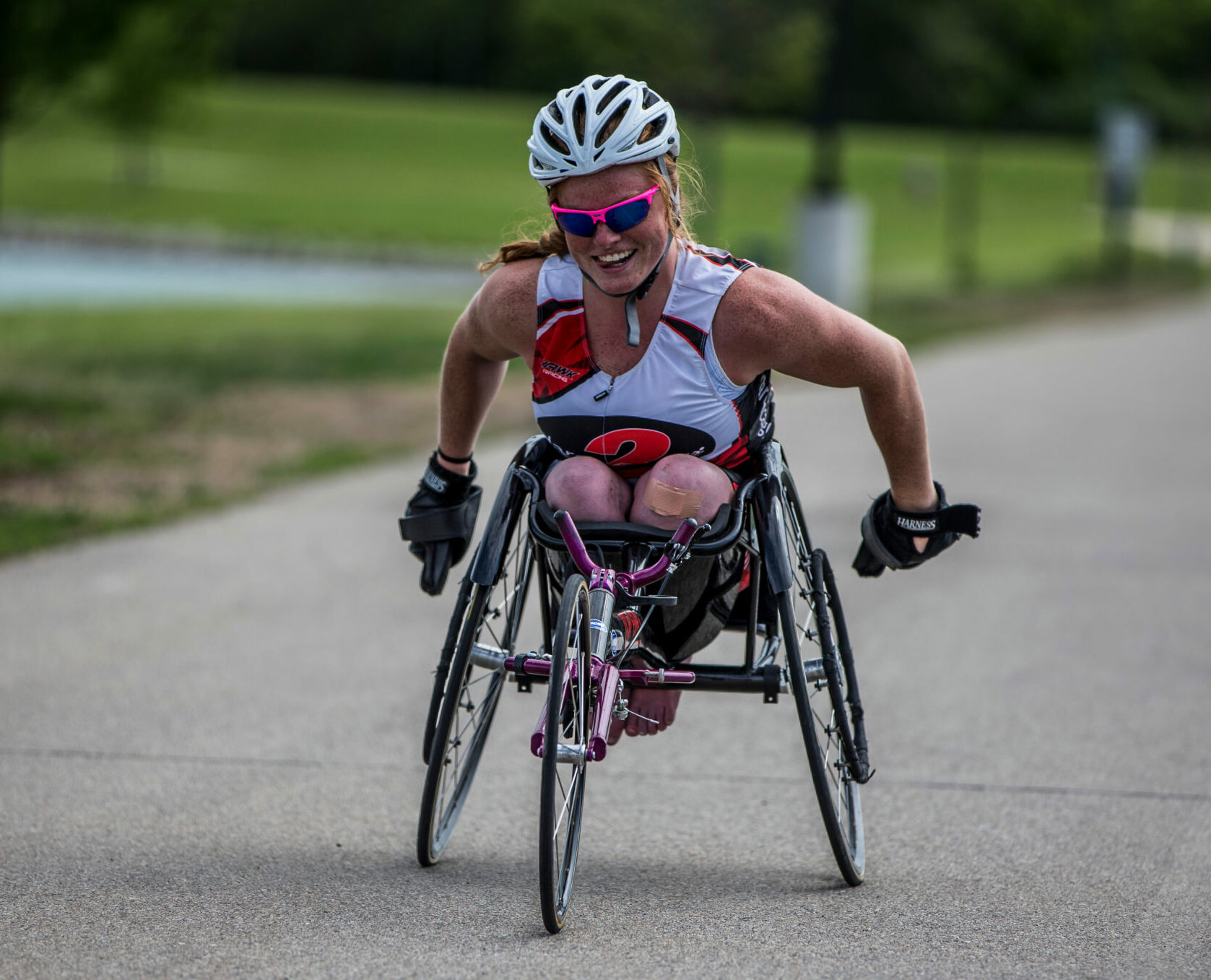 Athlete in racing chair racing on pavement towards photographer. Athlete is smiling