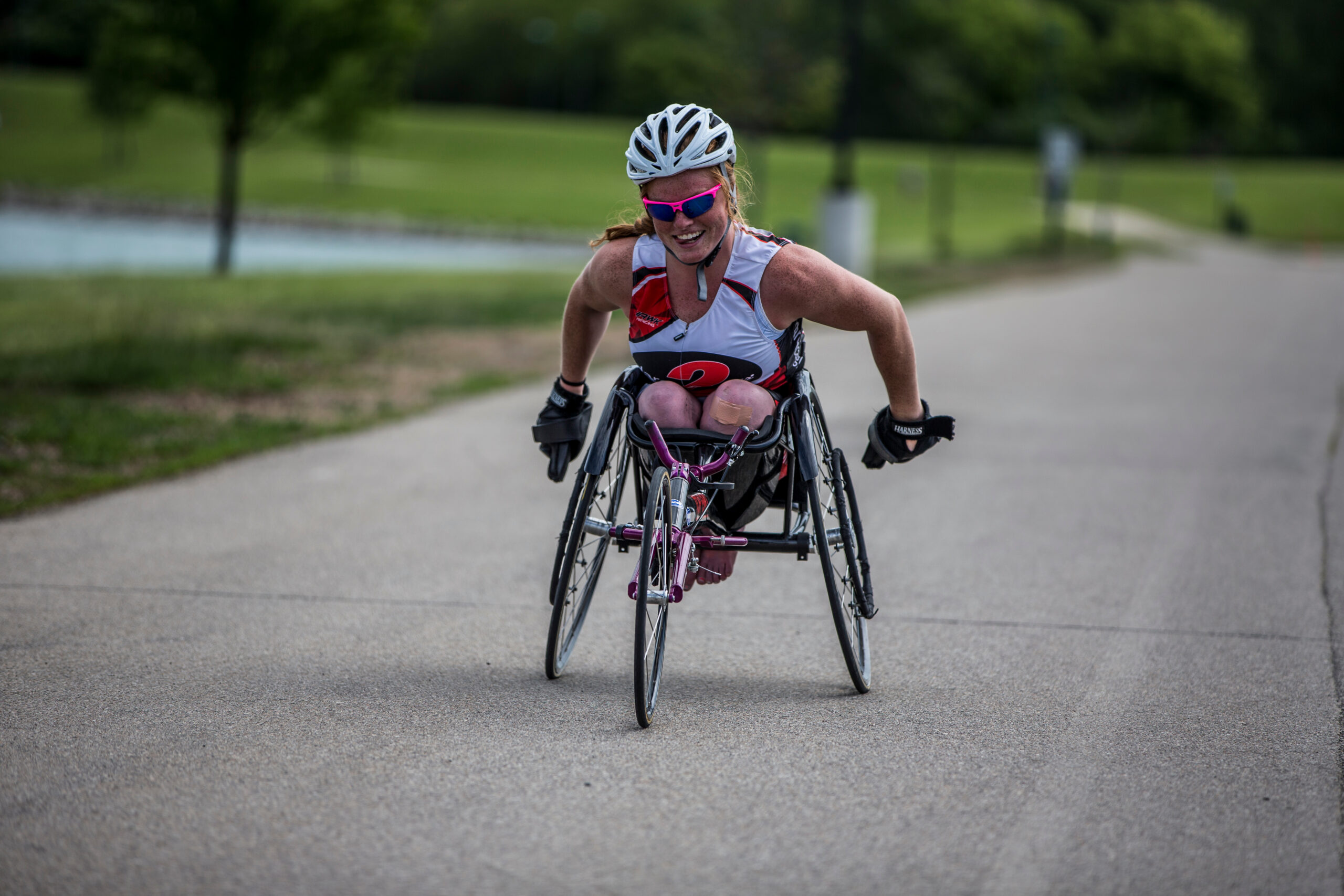 Athlete in racing chair racing on pavement towards photographer. Athlete is smiling