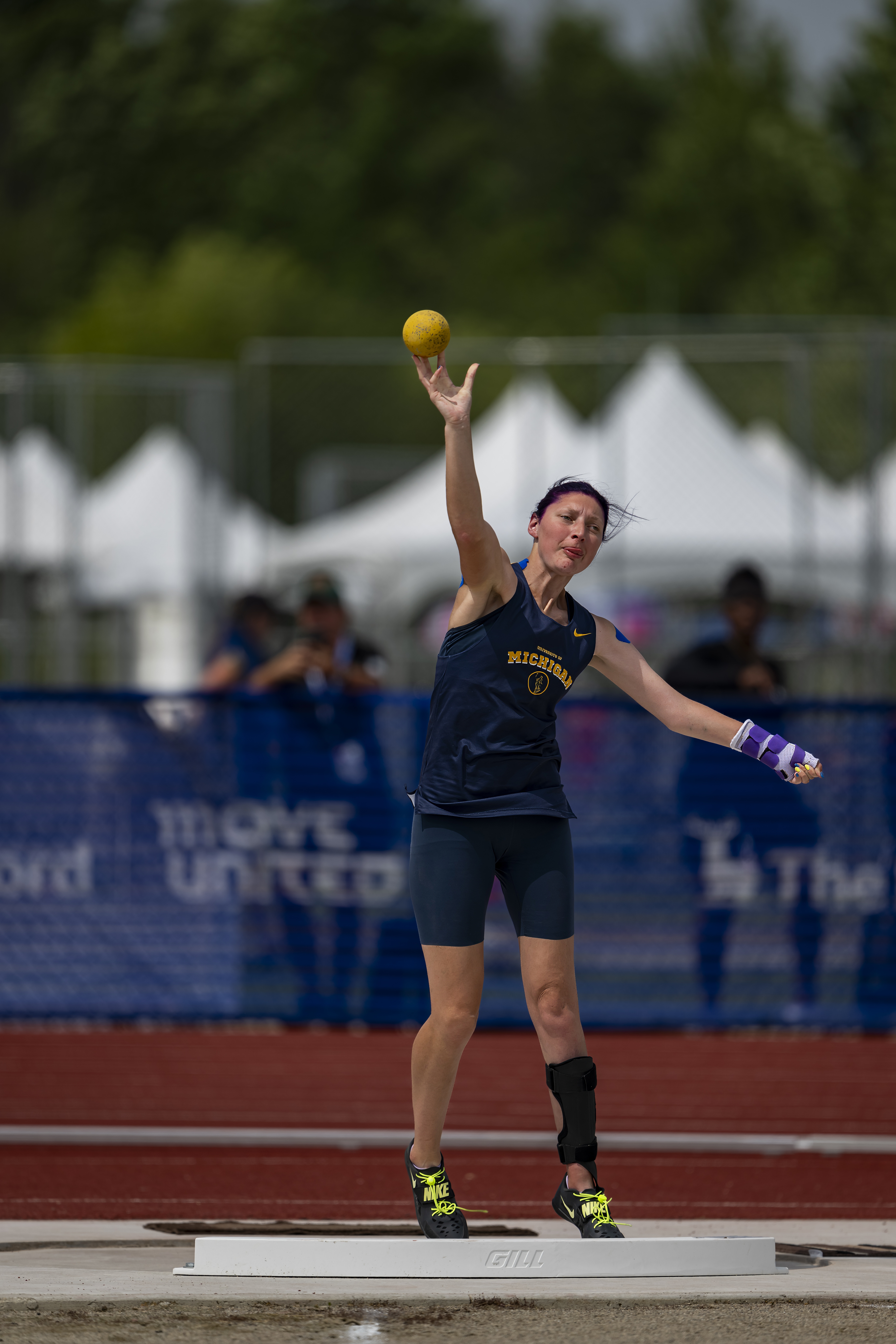 Athlete wearing Michigan jersey mid throwing shotput