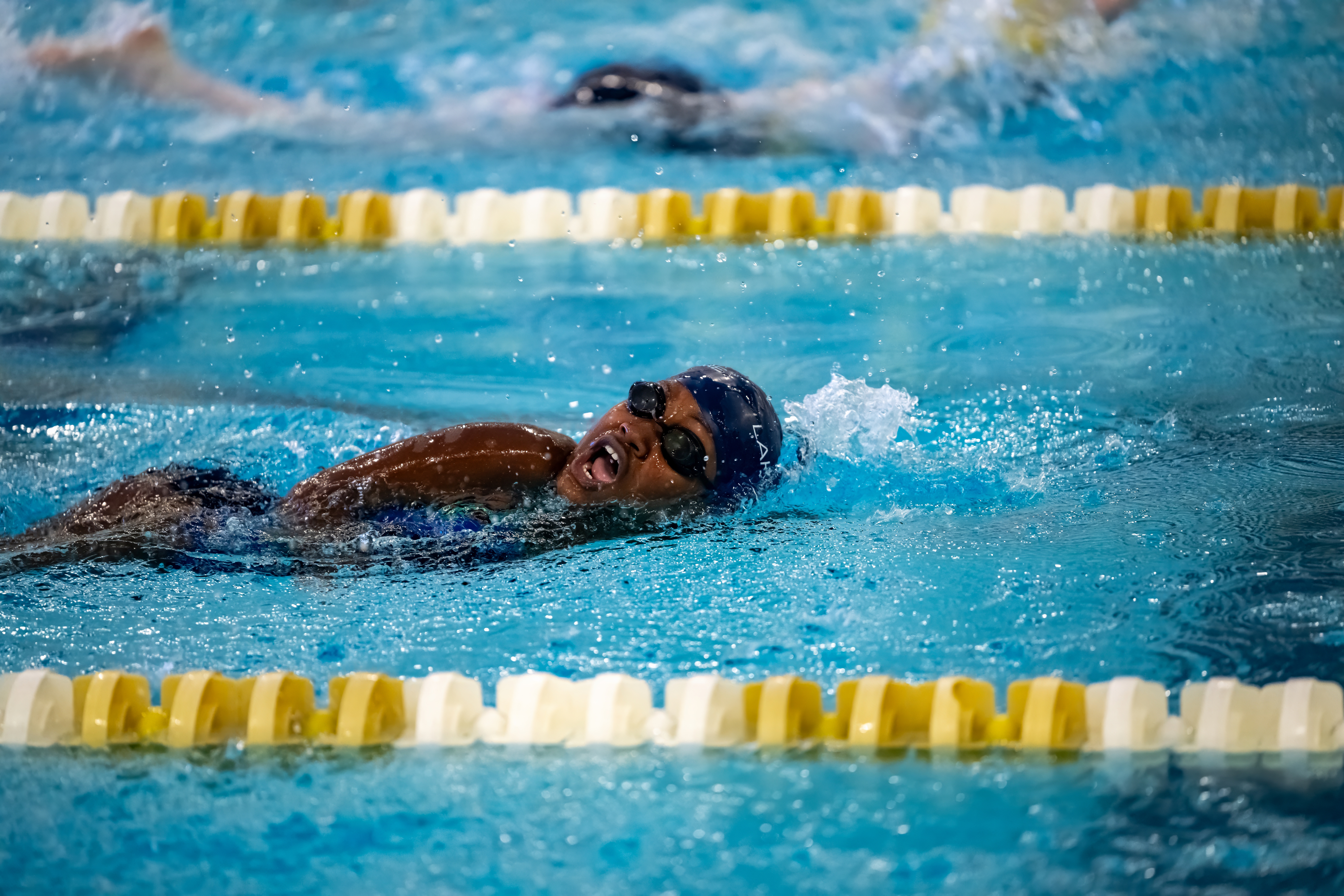 Athlete mid-freestyle stroke mid-race taking a breath. Athlete is wearing Lakeshore swim cap