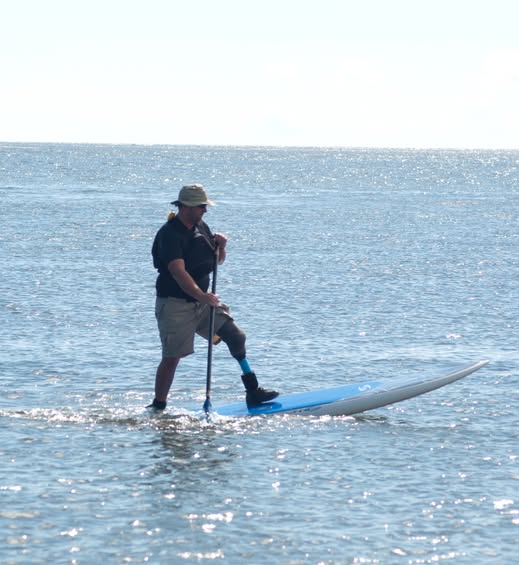 Joe Moore is standing on a paddle board and paddling out in the middle of a large body of water.