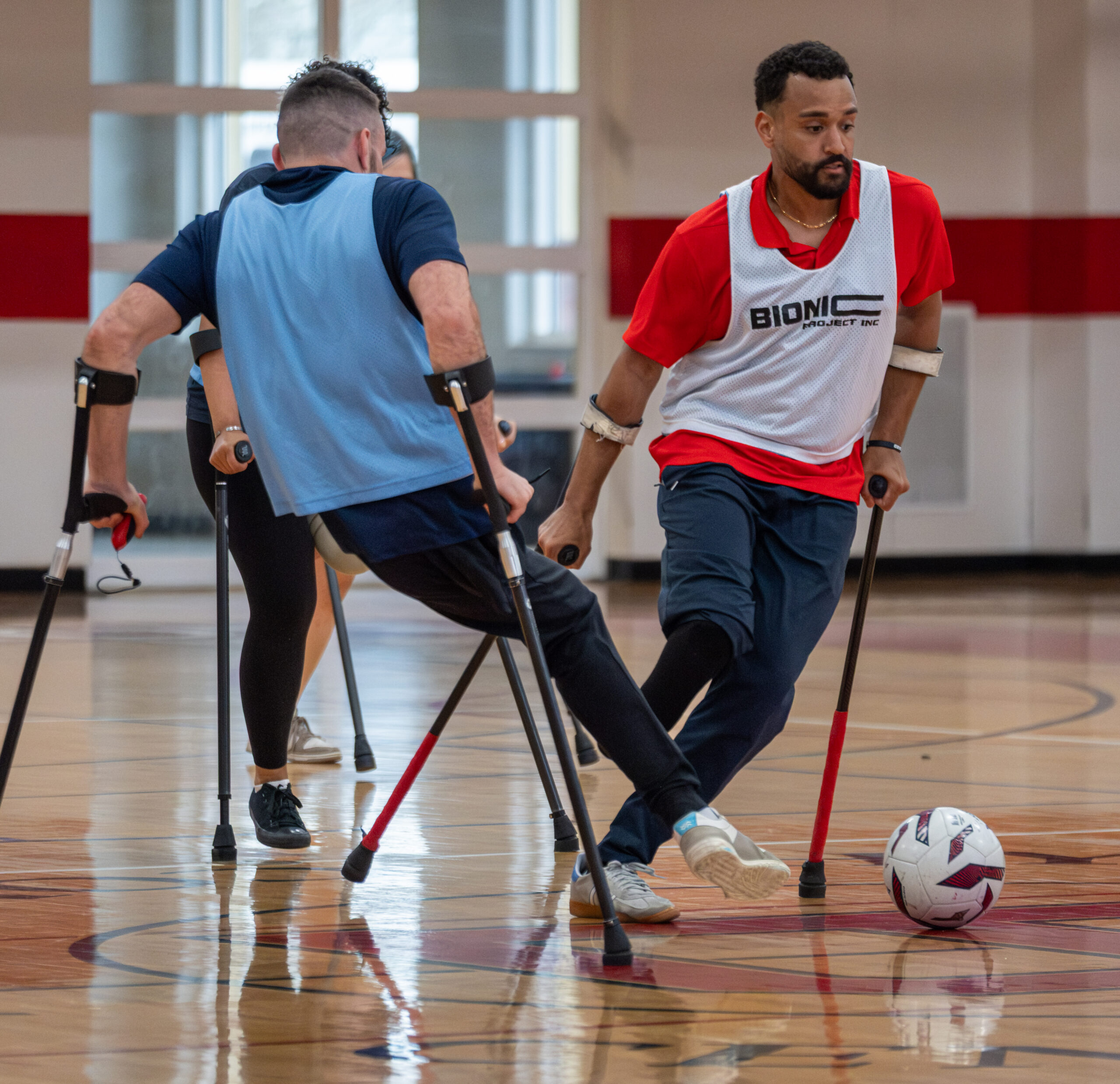 Two amputee athletes competing on gymnasium court facing off for the soccer ball.