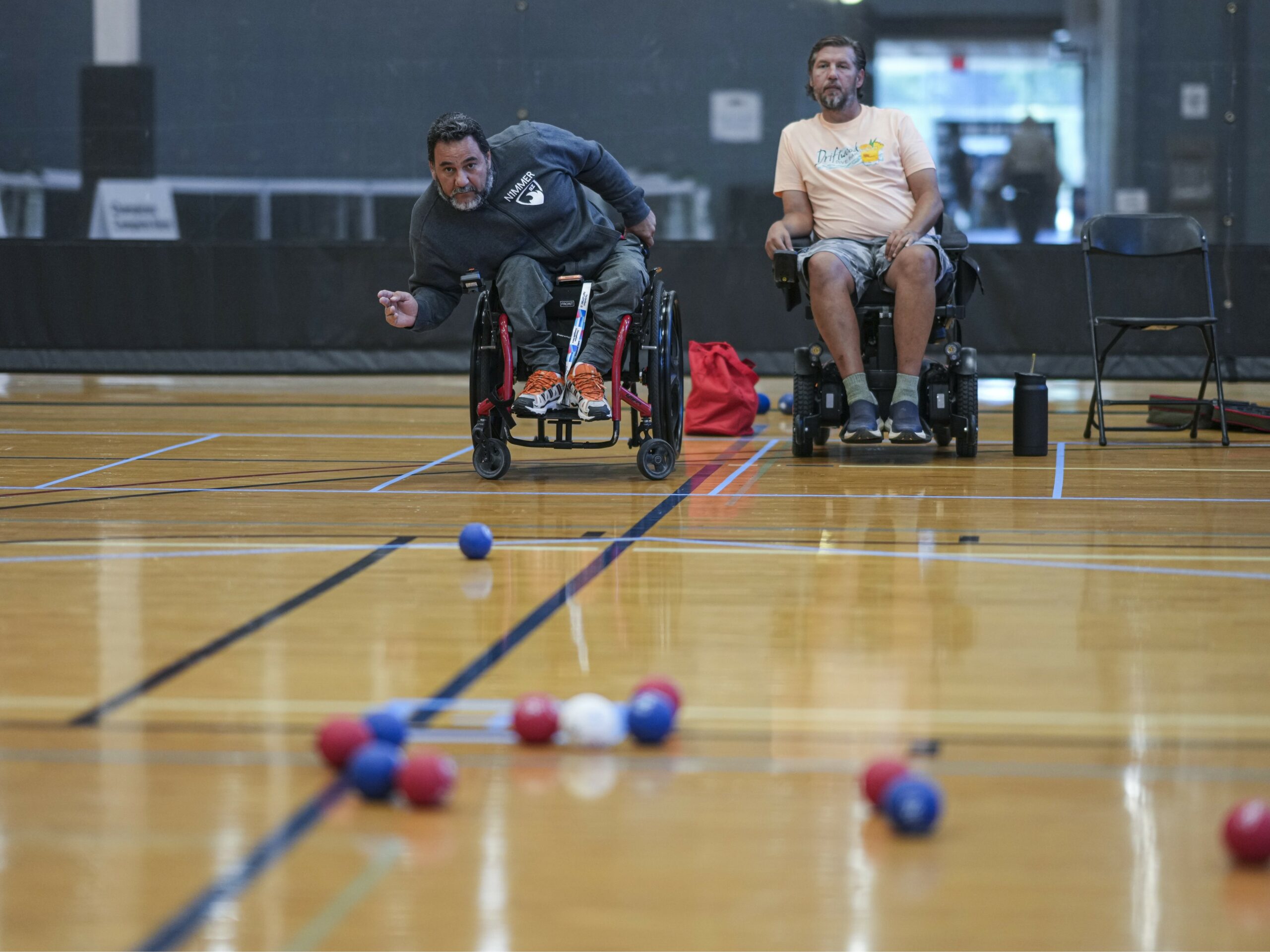 Two male adaptive athletes in wheelchairs playing boccia
