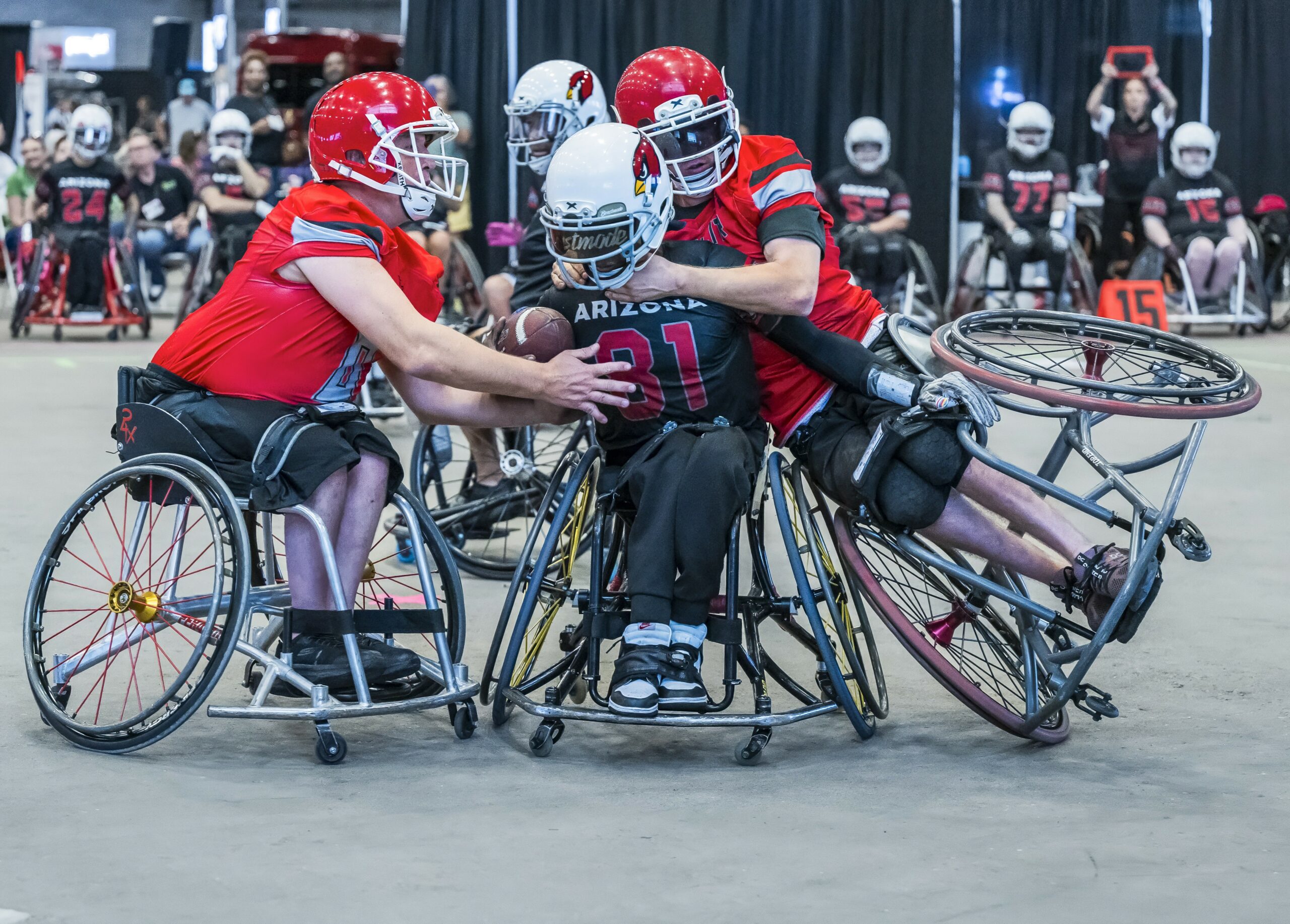 Wheelchair football players move in to tackle their opponent who has the ball