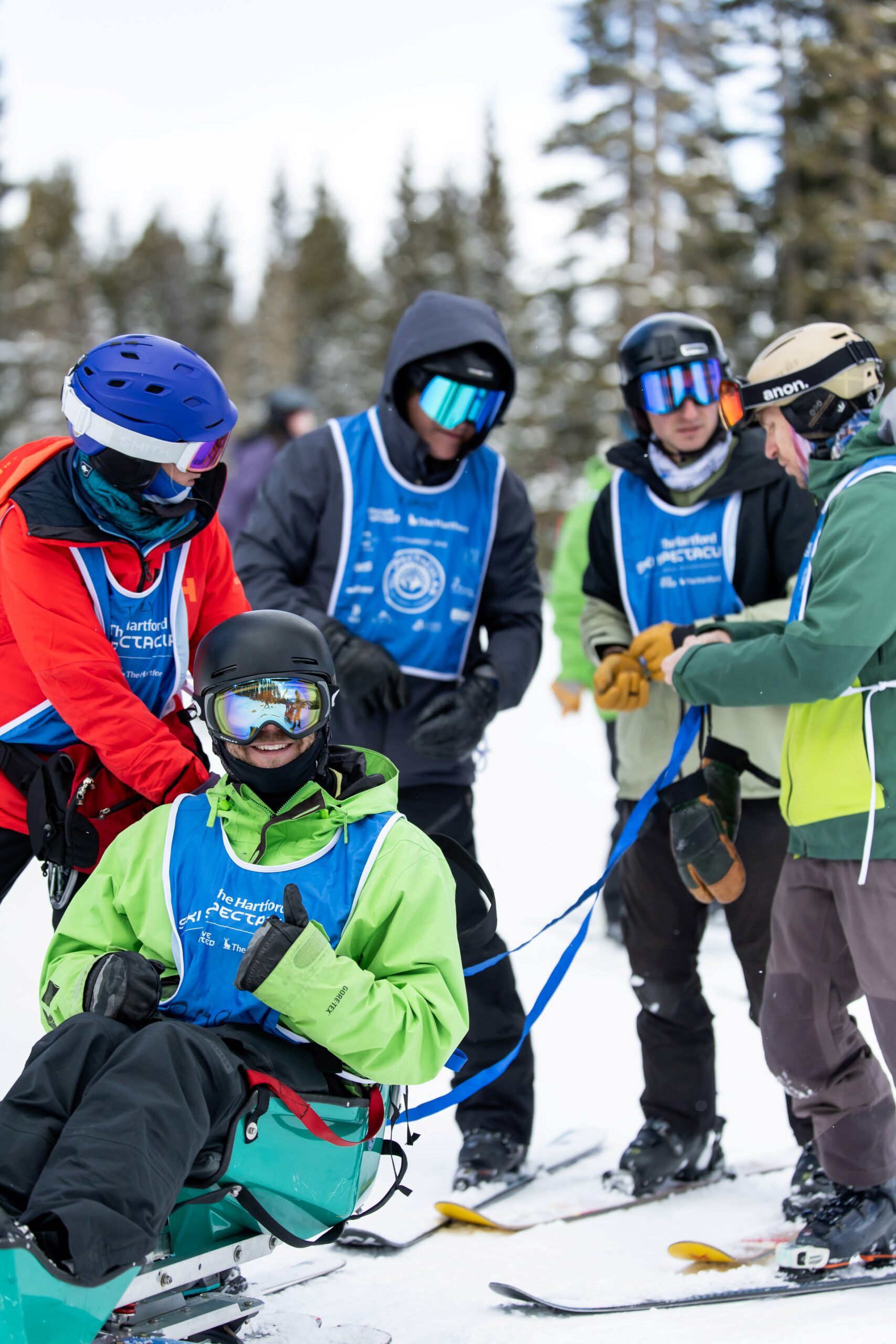 one male sit skier has an instructor and three student instructors behind him with a tether