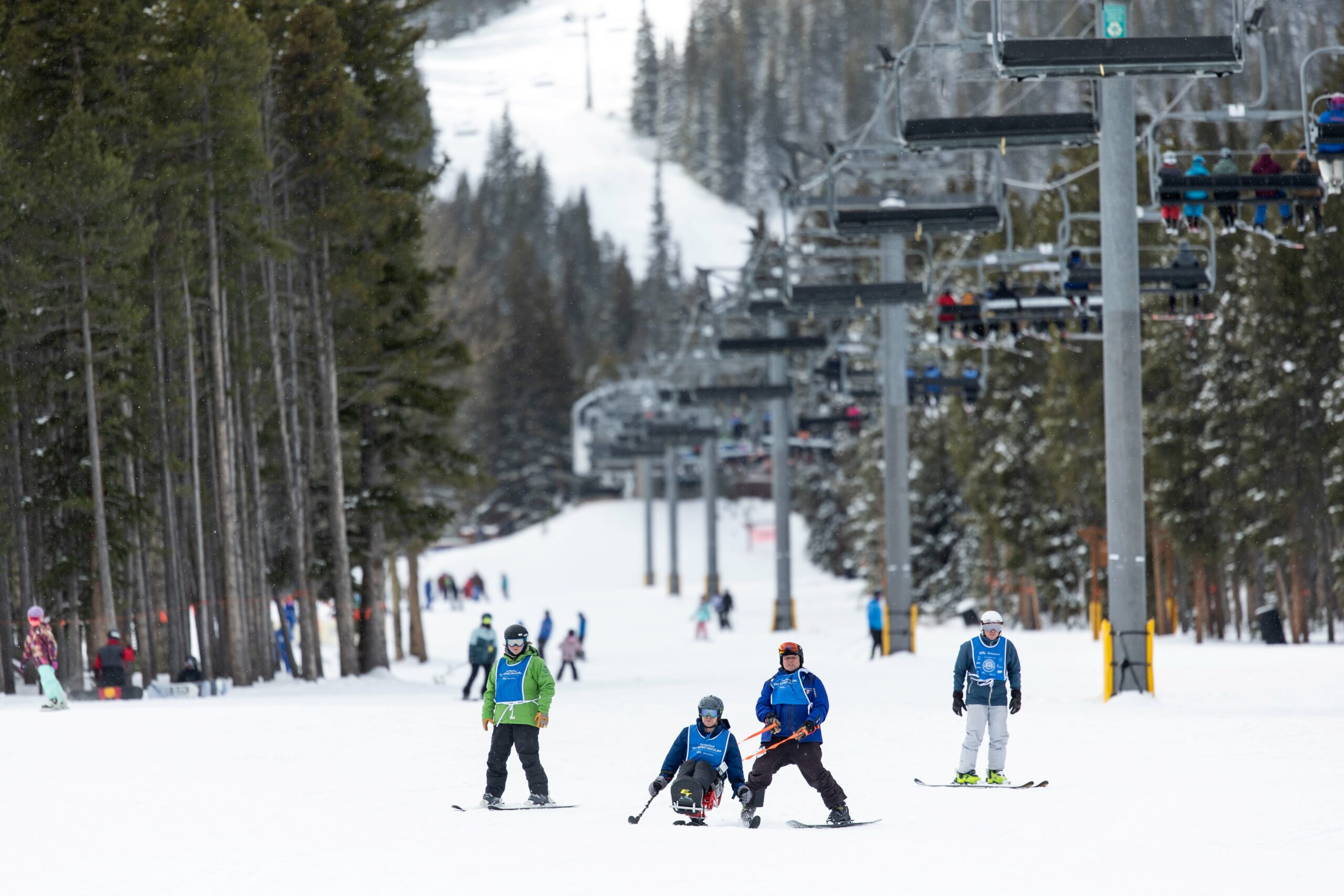 sit skier being tethered by an instructor with two additional instructors trailing them