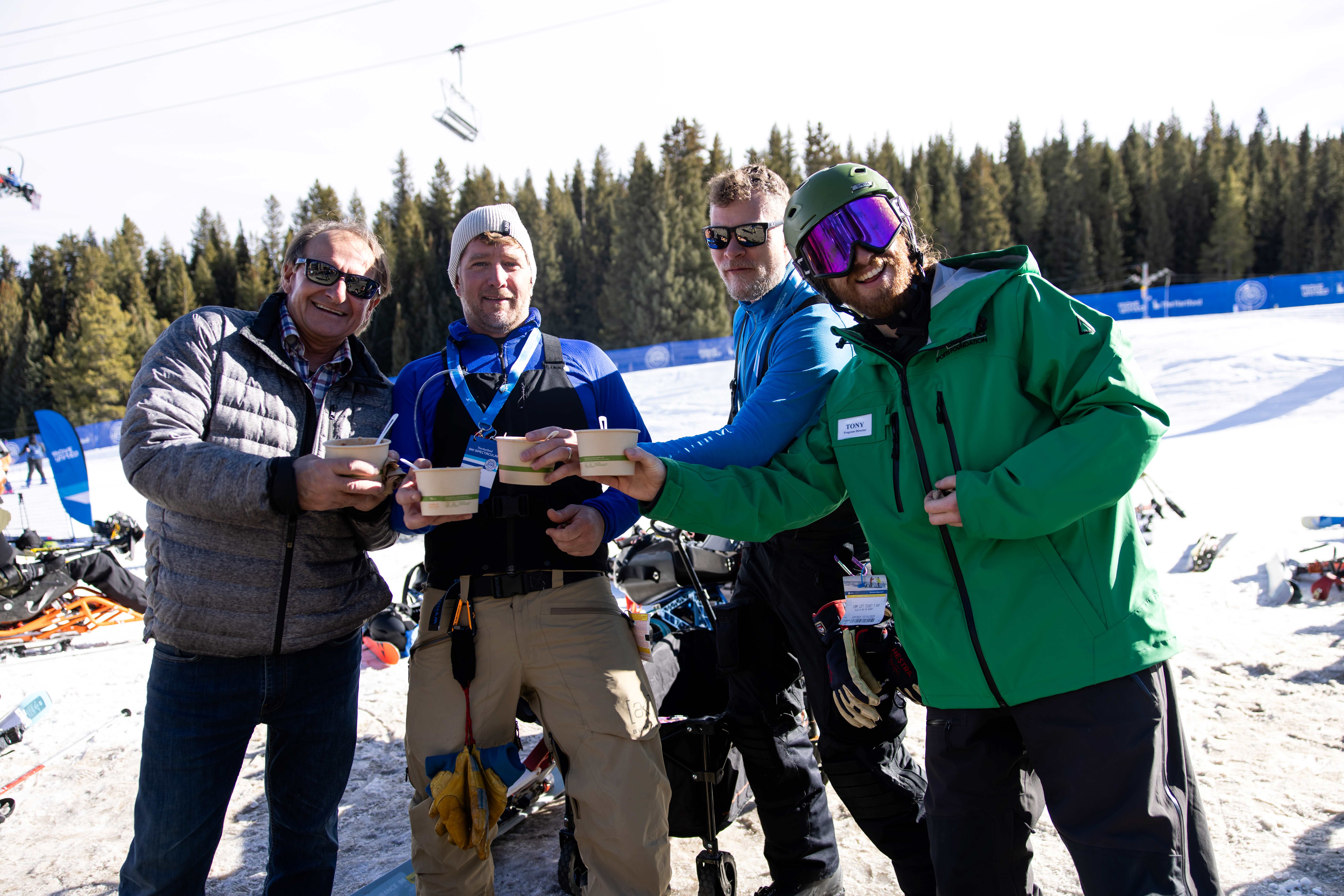 four adults standing together at the base of a ski slope holding soup