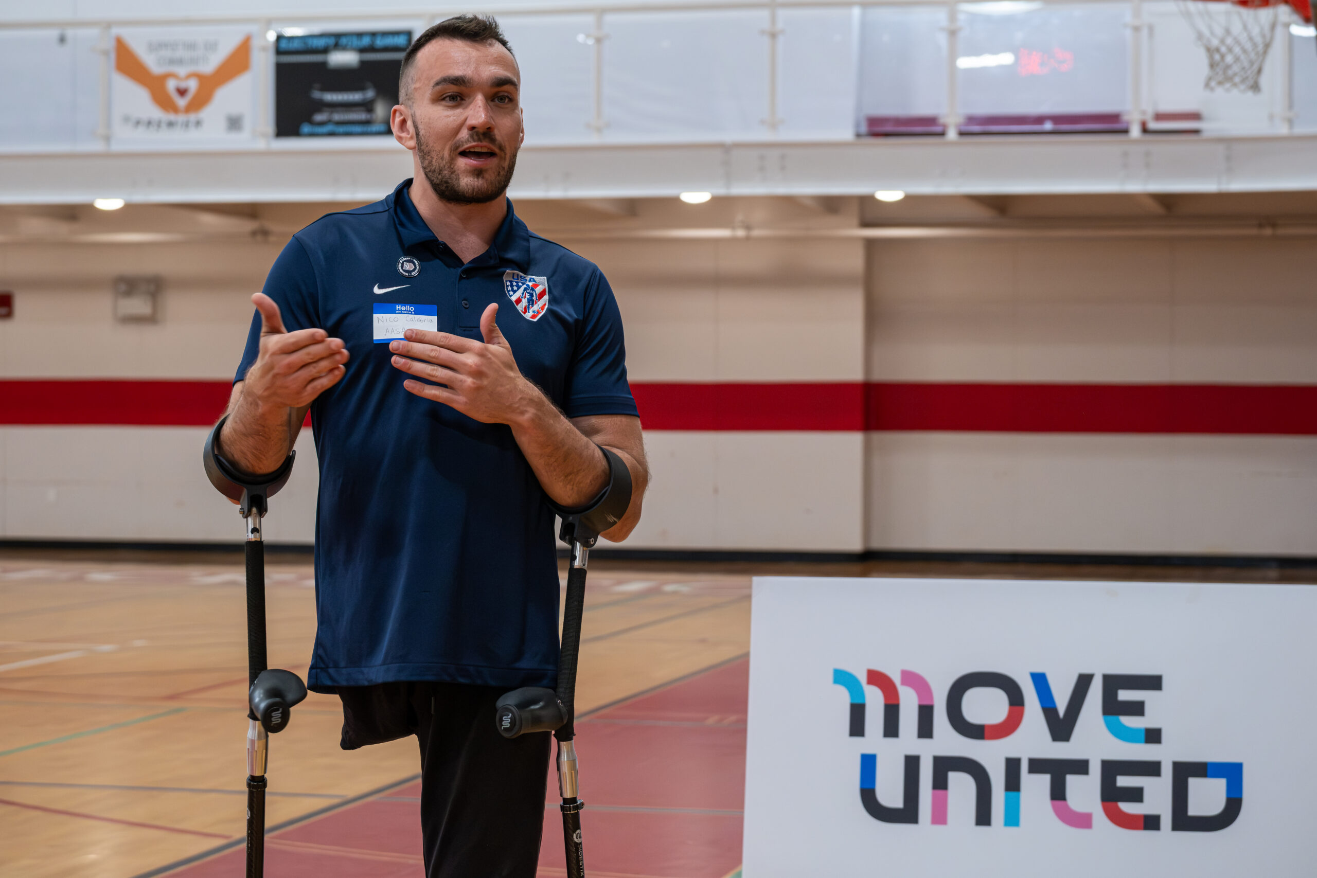 Amputee soccer player and presenter speaking, motioning with hands as he stands on sport court