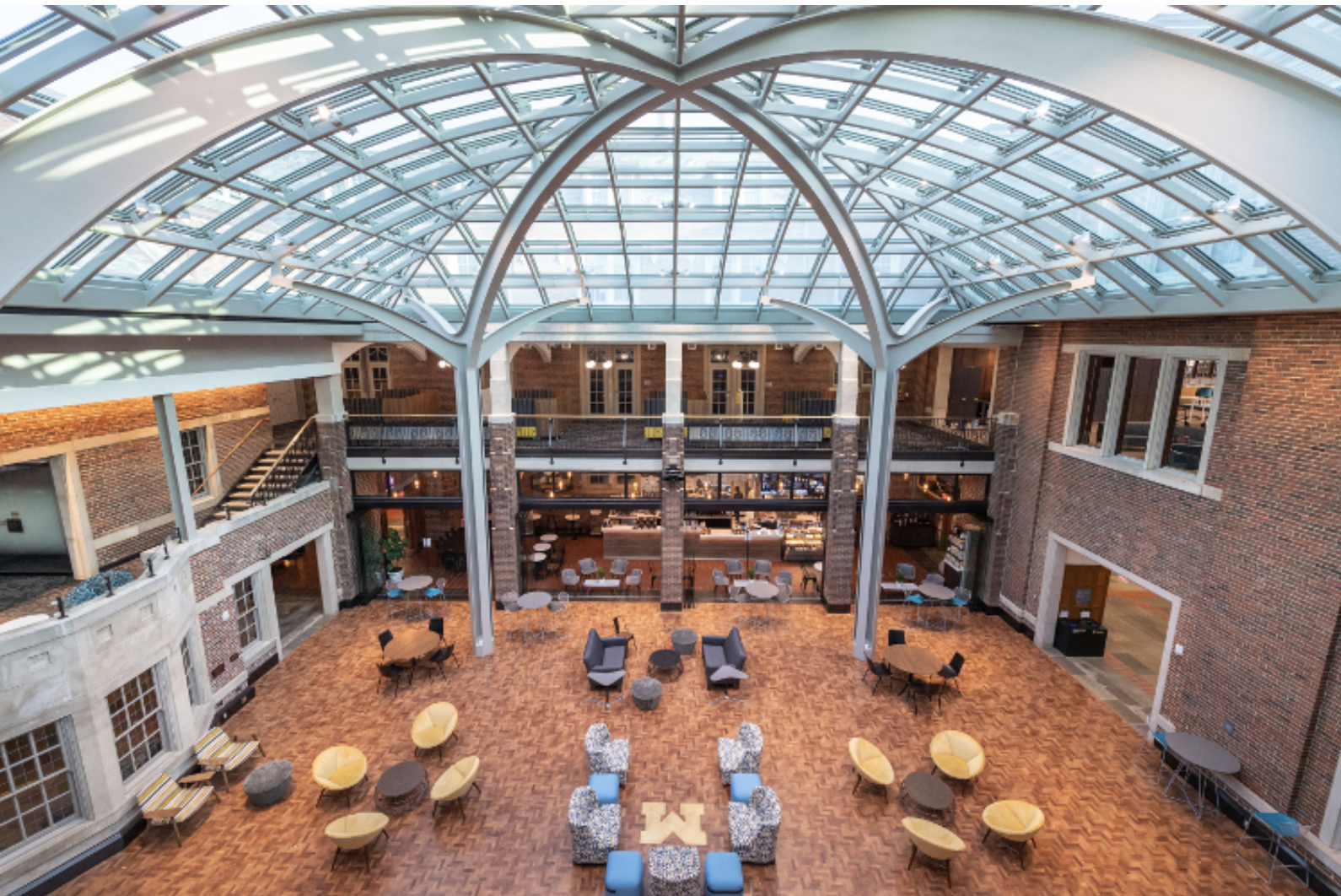 Large room with high glass ceilings, multiple tables with chairs, desks, and another level to view from sitting area.