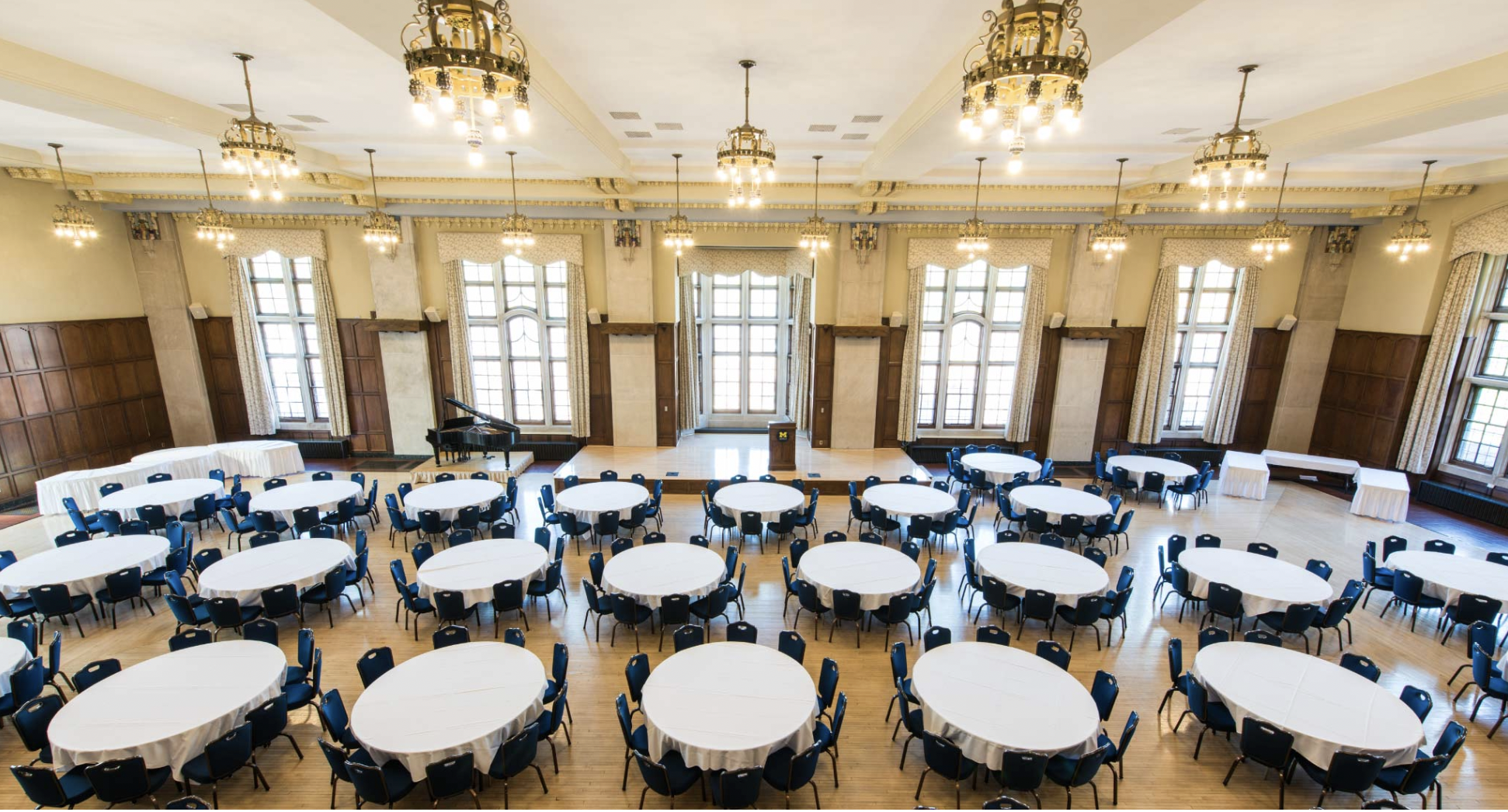 Ballroom with many tables, white tablecloths and chairs at each. This will be for meals.