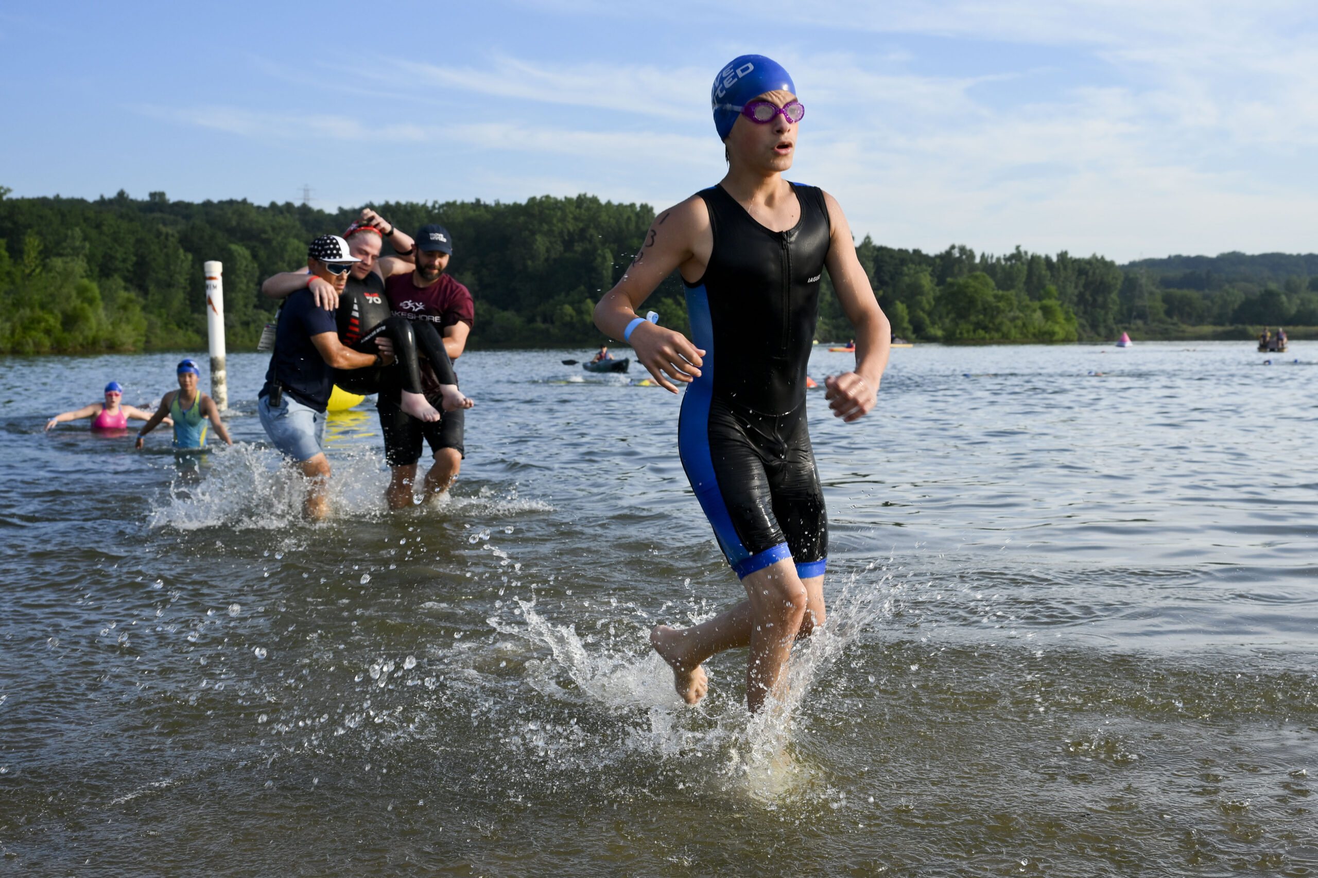 Athletes exiting the water after the swim portion of the paratriathlon. One athlete is being carried by two handlers.
