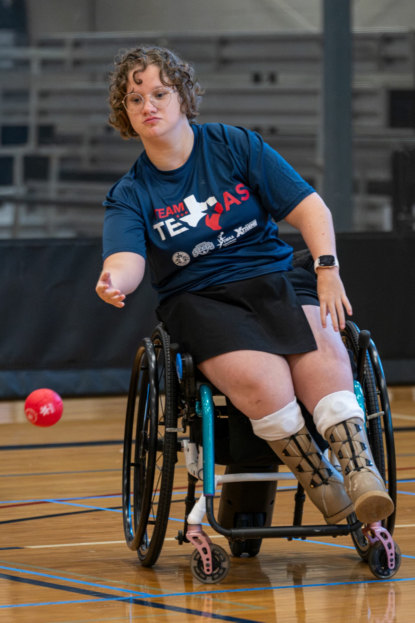 Athlete using a wheelchair throwing red ball in competitive boccia game