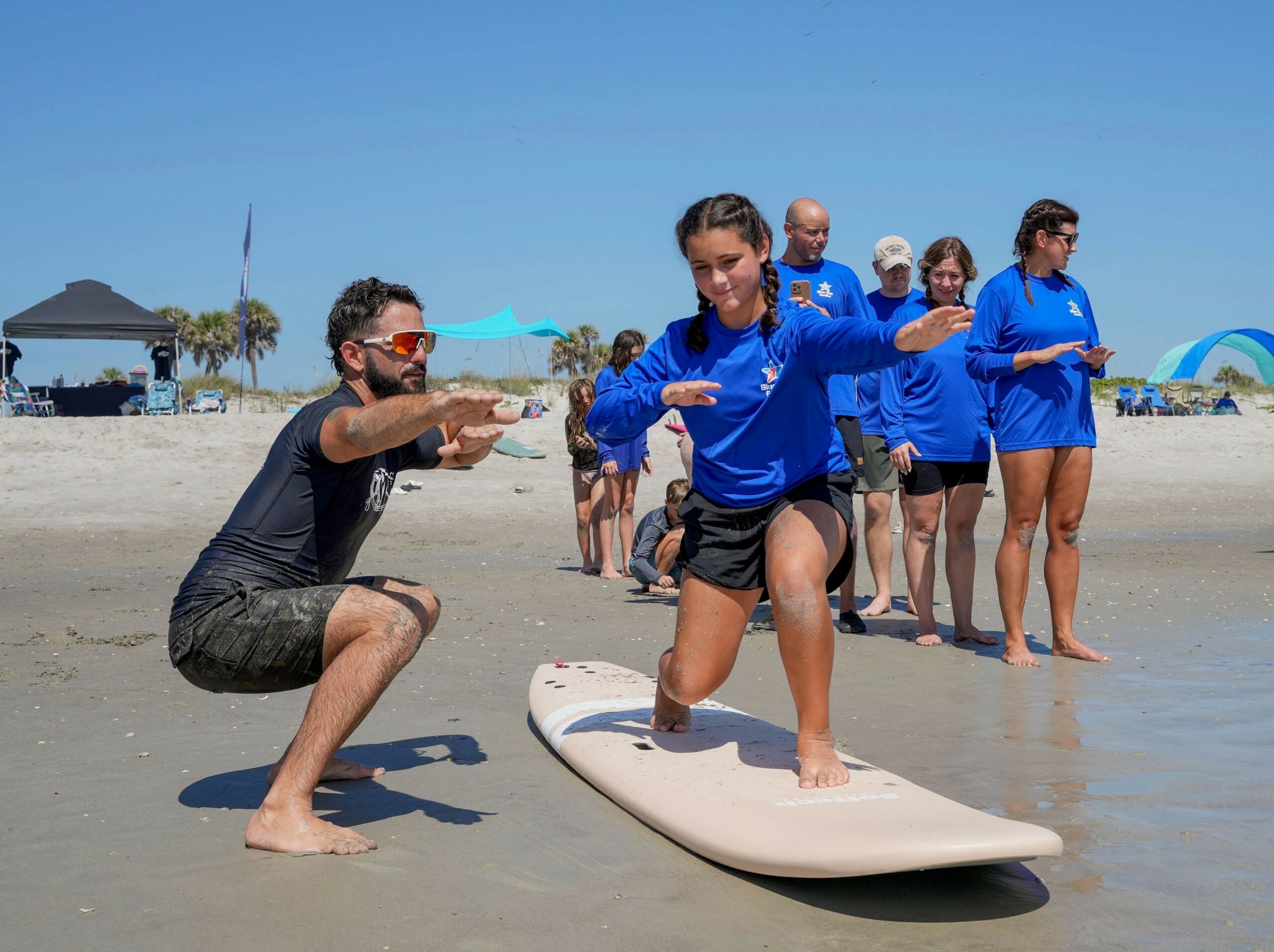 Patrick instructs a new surfboarder on the beach next to the ocean