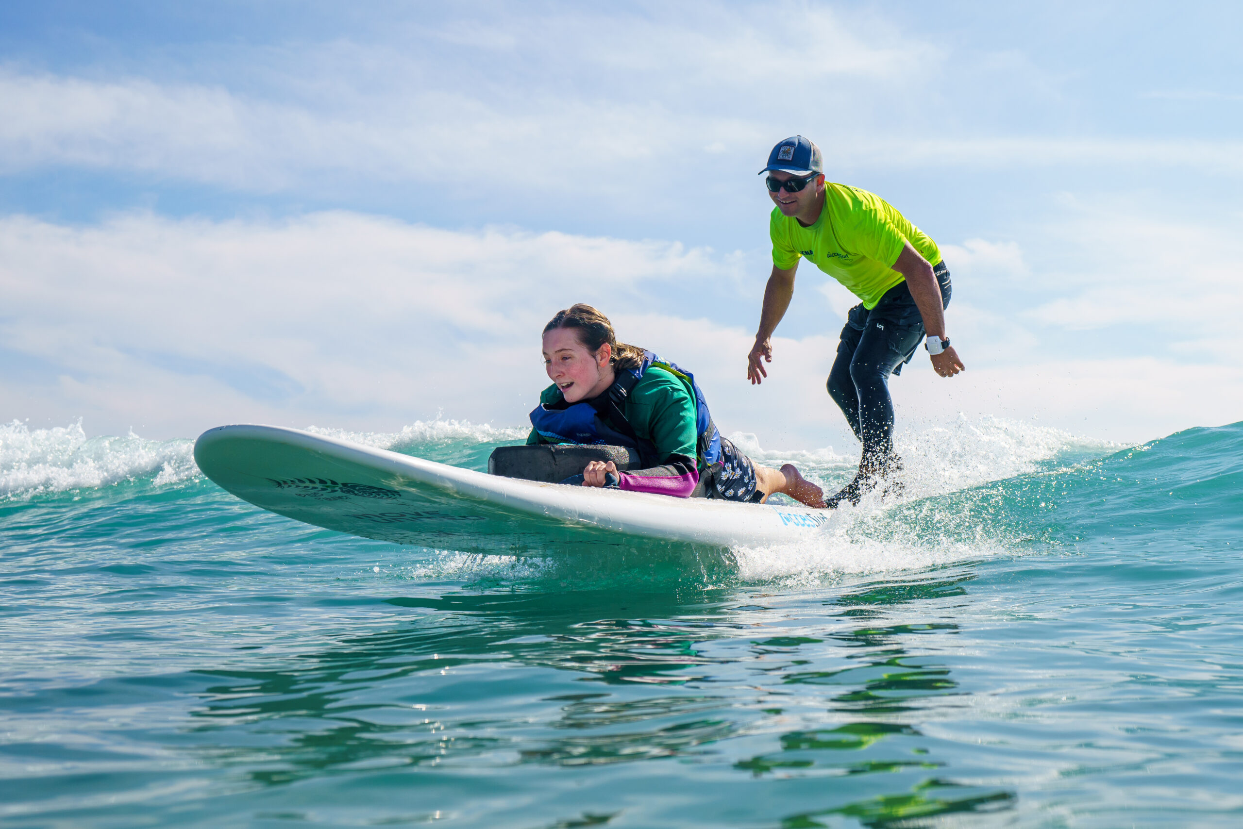 Individual prone on a surfboard riding a wave tandem with an instructor